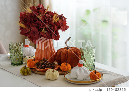 Thanksgiving table setting with decorative pumpkins, candles and string lights on white wooden table 129482836