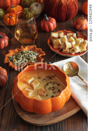 Creamy pumpkin soup with croutons and seeds, served in a pumpkin-shaped bowl on dark wooden table. 129482849