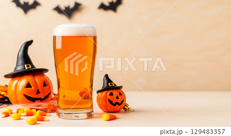 Halloween beer glass with pumpkin decorations, candy corn, and spooky bats on a festive holiday background. 129483357
