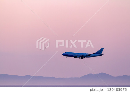 ピンク色の夕空を飛ぶ旅客機シルエット 129483976