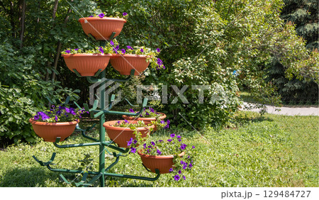 A beautiful multi-tiered metal stand for flower pots, in a park, outdoors A beautiful multi-tiered metal stand for flower pots, in a park, outdoors 129484727