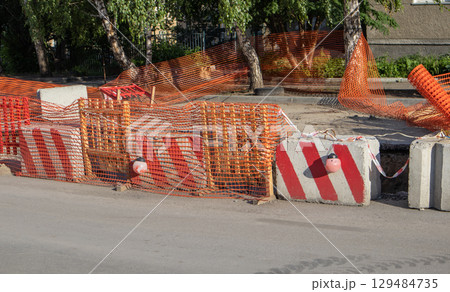 Painted concrete blocks, guardrails and orange mesh serve as safety barriers during road repairs 129484735