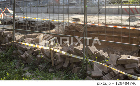 Excavated section of street during repair of underground heating system, surrounded by temporary fence. Pile of construction debris in the foreground Excavated section of street during repair of underground heating system, surrounded by temporary fence. Pile of construction debris in the foreground 129484746