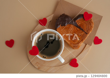 Coffee latte cappuccino drink beverage morning breakfast Heart shaped dark chocolate croissant on beige background with copy space. Puff pastry new trendy sweet dessert bakery. Creamy dough Coffee latte cappuccino drink beverage morning breakfast Heart shaped dark chocolate croissant on beige background with copy space. Puff pastry new trendy sweet dessert bakery. Creamy dough 129484800