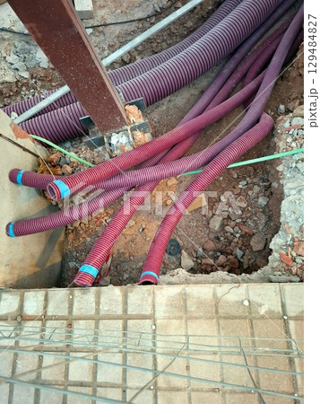 Many red plastic pipes are laid out in a construction site, ready for installation as part of the communication system. The groundwork indicates ongoing infrastructure development. 129484827