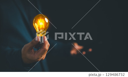 Businessman holding a glowing light bulb in a dark background, symbolizing creativity, creative solutions, innovation, and bright ideas. Business global internet connection application technology. Businessman holding a glowing light bulb in a dark background, symbolizing creativity, creative solutions, innovation, and bright ideas. Business global internet connection application technology. 129486732