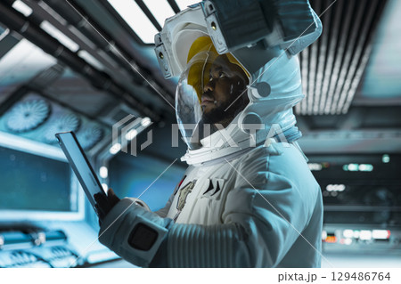 Astronaut using tablet, monitoring life support systems, conducting safety checks during long distance space travel. Starship crew member using device to verify navigation coordinates Astronaut using tablet, monitoring life support systems, conducting safety checks during long distance space travel. Starship crew member using device to verify navigation coordinates 129486764
