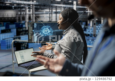 Data center admin using headset mic interpreting AI generated logs to resolve user issues. Technician identifying hardware issues using predictive AI alerts, guiding users Data center admin using headset mic interpreting AI generated logs to resolve user issues. Technician identifying hardware issues using predictive AI alerts, guiding users 129486792