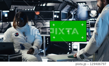 Researchers flying together in starship, looking at green screen monitor, exploring Mars. Cosmonauts using mockup display to ensure operational readiness before landing on red planet Researchers flying together in starship, looking at green screen monitor, exploring Mars. Cosmonauts using mockup display to ensure operational readiness before landing on red planet 129486797