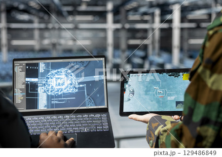 Close up of military operator and IT expert in army data center using AI on laptop to manage autonomous defense systems. Soldier and programmer using AI for strategic threat detection Close up of military operator and IT expert in army data center using AI on laptop to manage autonomous defense systems. Soldier and programmer using AI for strategic threat detection 129486849