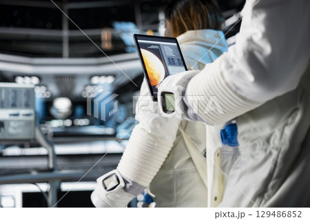 Close up of cosmonaut studying mission plans on device before Mars expedition, preparing for future of mankind. Astronaut in spaceship explores red planet to support human life beyond Earth Close up of cosmonaut studying mission plans on device before Mars expedition, preparing for future of mankind. Astronaut in spaceship explores red planet to support human life beyond Earth 129486852