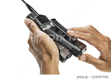 Closeup view of a human hand putting off the battery of a black walkie talkie radio communication device isolated over a white background Closeup view of a human hand putting off the battery of a black walkie talkie radio communication device isolated over a white background 129487509