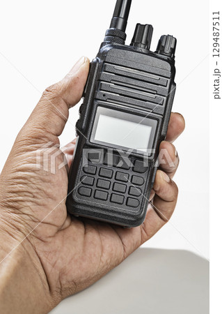 Closeup view of a human hand holding a black walkie talkie radio communication device isolated over a white background Closeup view of a human hand holding a black walkie talkie radio communication device isolated over a white background 129487511