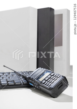 Closeup view of a black walkie talkie radio communication device and a computer keyboard on the table with a white background Closeup view of a black walkie talkie radio communication device and a computer keyboard on the table with a white background 129487516
