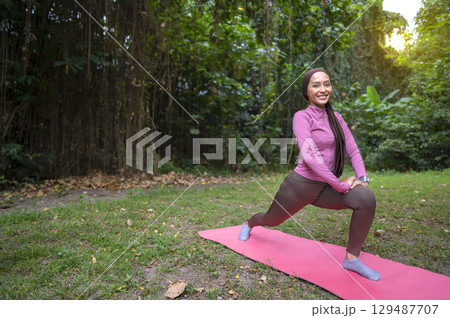 Indonesian southeast asian woman in a sporty outfit practices yoga on a fitness mat in a public park outdoors. Concept of a Healthy active lifestyle Indonesian southeast asian woman in a sporty outfit practices yoga on a fitness mat in a public park outdoors. Concept of a Healthy active lifestyle 129487707