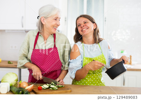 Senior woman and her daughter cooking dinner together 129489083