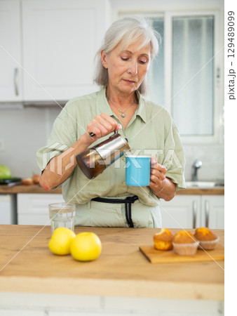 Old woman pouring coffee, having breakfast at home Old woman pouring coffee, having breakfast at home 129489099