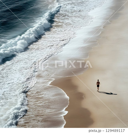Man jogging near ocean waves rolling over sandy beach, capturing peaceful seaside morning landscape with tranquil coastal atmosphere 129489117