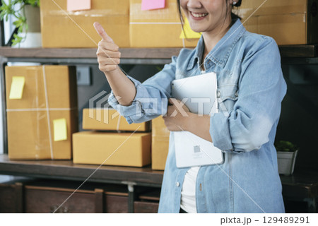 Asian woman startup small business at home office. Online seller entrepreneur young asian woman use tablet checking online order. Woman using tablet check stock goods supply delivery package shipping Asian woman startup small business at home office. Online seller entrepreneur young asian woman use tablet checking online order. Woman using tablet check stock goods supply delivery package shipping 129489291
