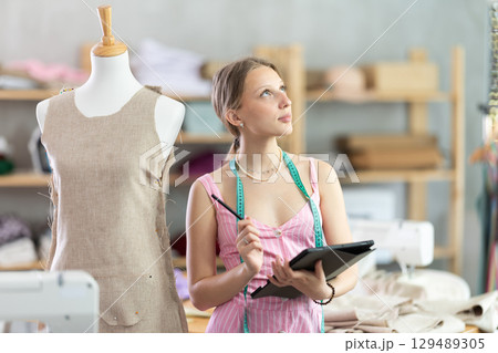 Young female dressmaker drawing in tablet in sewing workshop Young female dressmaker drawing in tablet in sewing workshop 129489305