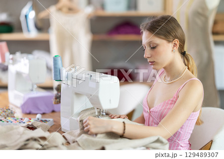 Woman seamstress sews on sewing machine in workshop 129489307