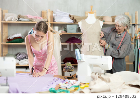 young dressmaker helps a seamstress with sewing clothes 129489332