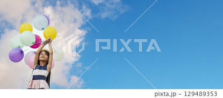 Banner Cheerful cute girl holding balloons running green meadow white cloud and blue sky with happiness. Panorama Hands holding vibrant air balloons happy times summer sunlight outdoor copy space 129489353