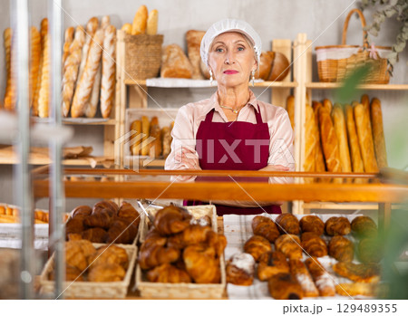 Senior female baker worker sells croissants, shows many different crescent rolls Senior female baker worker sells croissants, shows many different crescent rolls 129489355