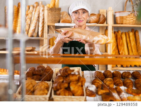 Elderly female bakery salesperson offers to buy bread, baguettes and croissants Elderly female bakery salesperson offers to buy bread, baguettes and croissants 129489358