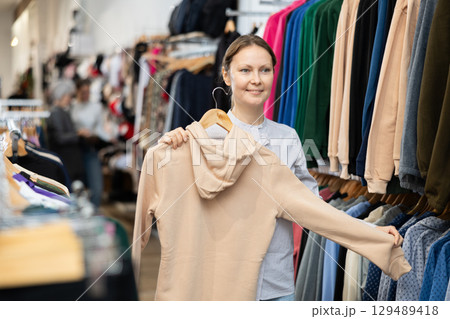 Middle-aged woman choosing convenient hoodie in clothing store 129489418