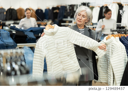 Old woman choosing white jacket in clothing store 129489437
