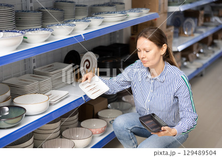Woman in supermarket is choosing square plates 129489504