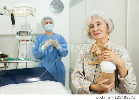 Smiling woman holding with bandaged belly after successful surgery 129489573