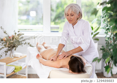 Elderly woman doing back massage to young woman 129489883