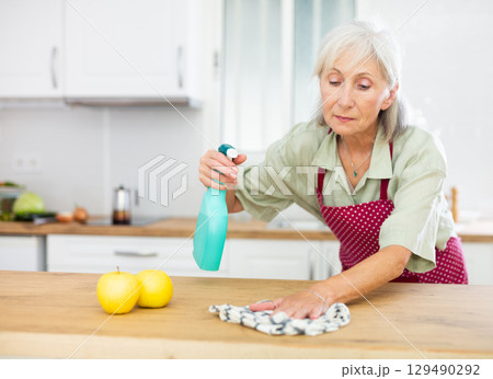 Senior woman washing kitchen table during cleanup 129490292