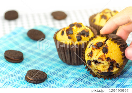Fresh homemade delicious vanila and chocolate muffins in paper cupcake holder with cookie and cream isolated on napkin, tablecloth in background. 129493995