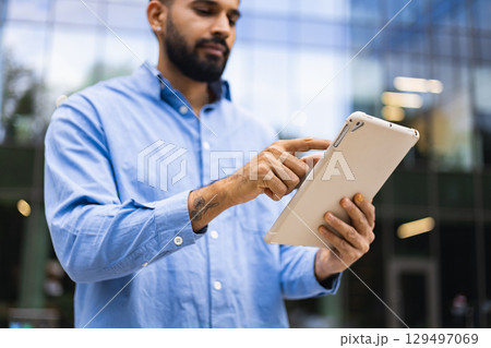 A man with a beard is using a tablet outdoors in front of a building. A man with a beard is using a tablet outdoors in front of a building. 129497069