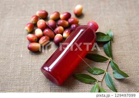 Vibrant Bottle of Red Liquid Surrounded by Fresh Fruits and Green Leaves on Natural Background 129497099