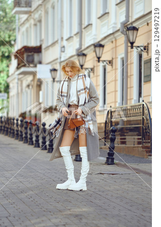 A young woman in an autumn outfit stopped on a street and is looking for something in her purse A young woman in an autumn outfit stopped on a street and is looking for something in her purse 129497219