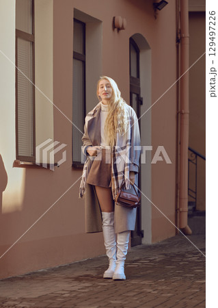 A young woman in a stylish autumn outfit stands on a city street during the golden hour 129497226