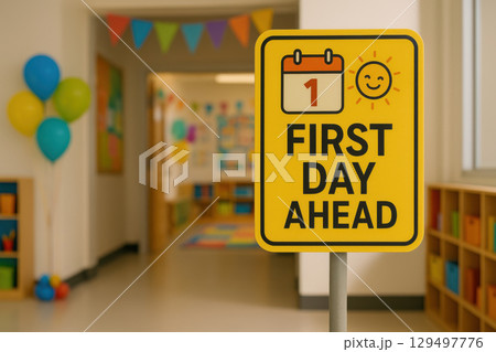 Colorful warning sign FIRST DAY AHEAD with calendar and smiling sun icon stands in cheerful classroom entrance decorated with balloons 129497776
