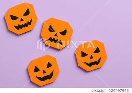 Origami pumpkin faces with creepy expressions arranged on pastel violet paper create minimalist Halloween craft theme Origami pumpkin faces with creepy expressions arranged on pastel violet paper create minimalist Halloween craft theme 129497946