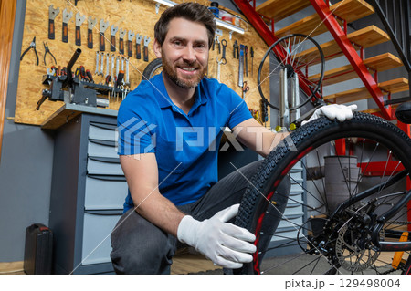 Confident male technician holding mountain bike wheel fixing tire in professional repair shop Confident male technician holding mountain bike wheel fixing tire in professional repair shop 129498004