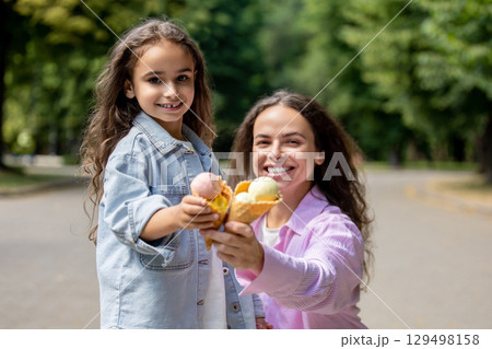 Smiling family mother with child enjoying frozen dessert together in park Smiling family mother with child enjoying frozen dessert together in park 129498158
