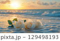 Soft White Roses on Sand at Sunrise with Ocean Waves and Gentle Light in Background 129498193