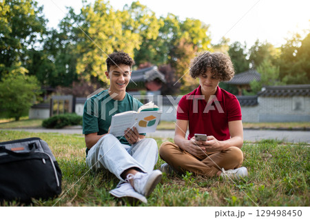 Two teens sitting on the grass and reading books while preparing for lessons 129498450