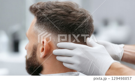 Man with fresh haircut is getting precise hair trim at beauty salon where skilled hands wearing gloves ensure clean and stylish look with care and professionalism 129498857