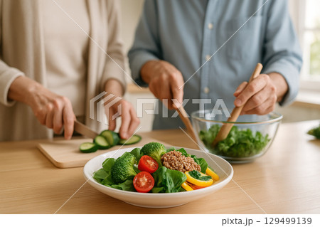 Healthy salad with fresh vegetables and grains on plate with two people preparing food together in background, creating warm and wholesome cooking atmosphere 129499139
