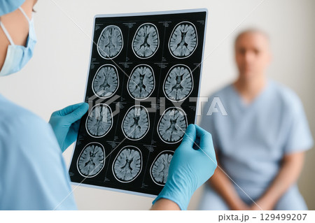 Brain MRI scan held by medical professional with patient in background showing brain scan for neurology diagnosis in clinical setting 129499207