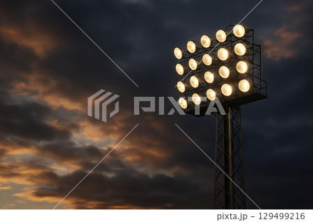 Stadium light tower glowing at dusk with dark cloudy sky creating dramatic atmosphere in soccer field and football stadium setting Stadium light tower glowing at dusk with dark cloudy sky creating dramatic atmosphere in soccer field and football stadium setting 129499216